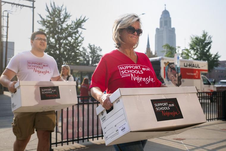 Noah Snurr of Nebraska State Education Association, left, and Molly Gross of Nebraska Parent Teacher Association deliver boxes of signatures from the Support Our Schools Nebraska petition drive to the Nebraska Secretary of State, Wednesday, Aug. 30, 2023, in Lincoln, Neb. Organizers of an effort to have Nebraska voters weigh in on whether to use taxpayer money to pay for private school tuition scholarships said Wednesday they have more than enough signatures to put that question on the November 2024 ballot. (Justin Wan/Lincoln Journal Star via AP)